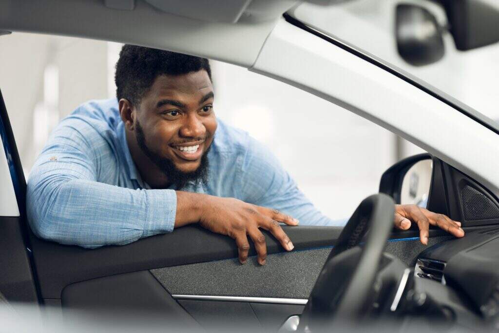 Homem na janela de um carro olhando feliz para dentro do veículo.