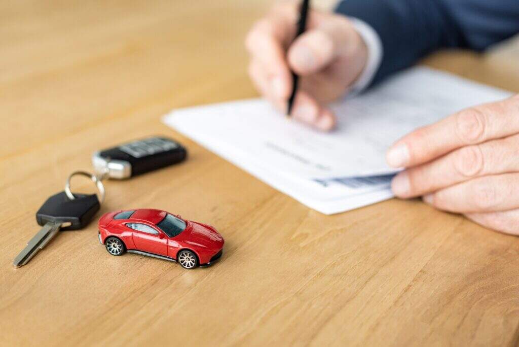 Homem conferindo tabela de seguro de carro em uma mesa, onde há uma chave e um carrinho de brinquedo.