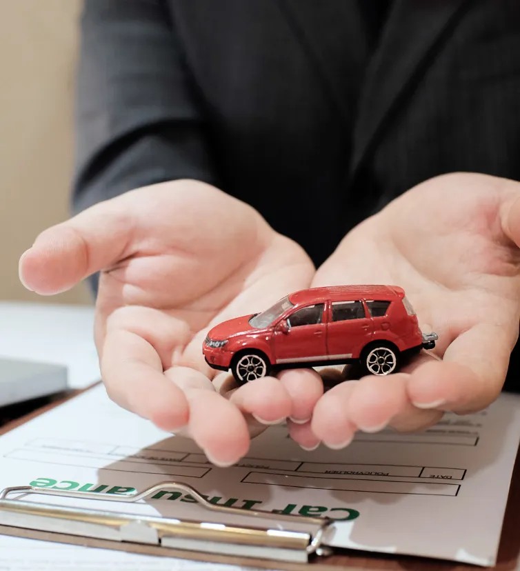 homem segurando um carro de brinquedo vermelho em suas duas mãos, abaixo das mãos tem uma apólice de seguros, mostrando como funciona uma corretora de seguros.