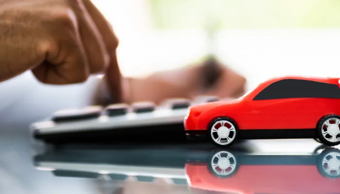 homem fazendo calculo em sua calculadora, com carro de brinquedo ao lado, representando a comparação entre financiamento vs consórcio de carros.