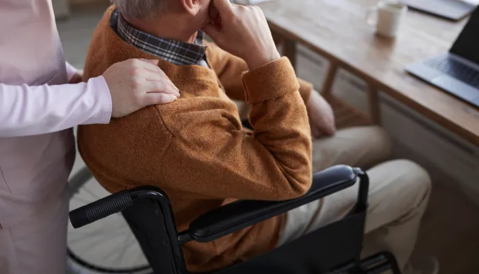 homem sendo cuidado por uma mulher, sentado e triste em uma cadeira de rodas, representando depressão e invalidez quando o seguro de vida entra em cena.
